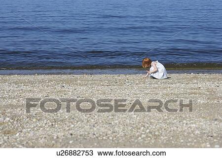 Stock Image - Young girl (5-6) squatting on beach. Fotosearch