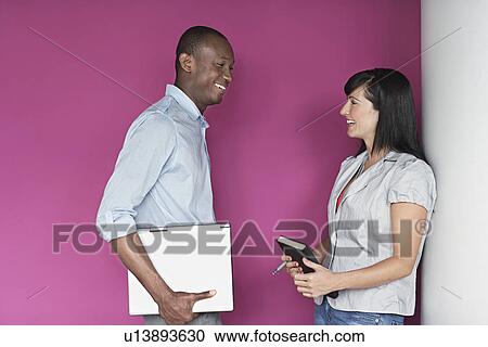 Stock Image - Young man and young woman talking by purple wall. Fotosearch
