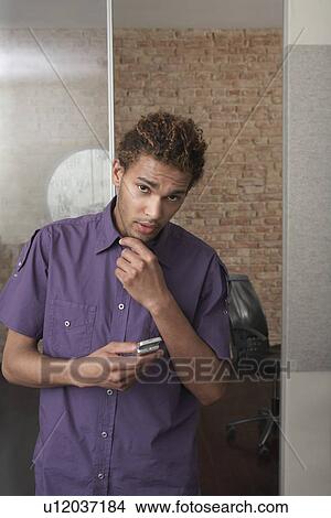 Picture - Young man holding mobile phone in office. Fotosearch