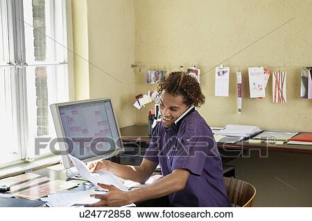 Young man reading papers and using phone in office View Large Photo Image Stock Photo - Young man reading papers and using phone in office. Fotosearch