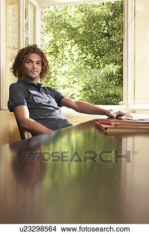 Picture - Young man sitting in living room near open window. Fotosearch