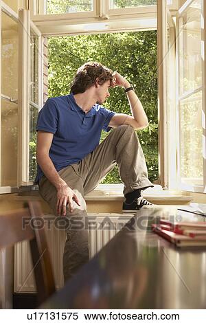 Young man sitting on sill looking out living room window View Large Photo Image Stock Photography - Young man sitting on sill looking out living room window. Fotosearch