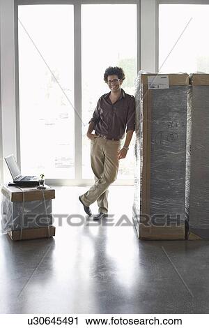 Young man standing by packages in empty office View Large Photo Image Stock Image - Young man standing by packages in empty office. Fotosearch