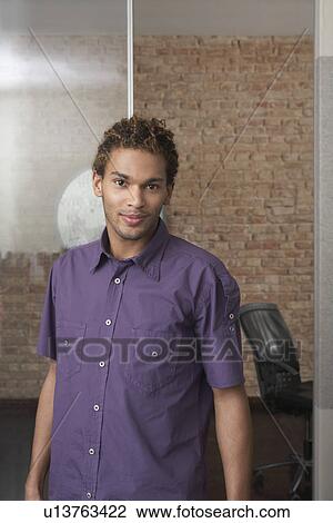 Stock Image - Young man standing in office. Fotosearch