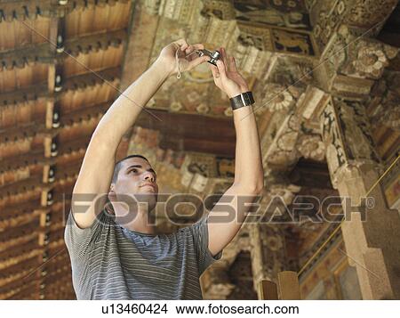 Picture - Young man taking photograph of wooden detail of temple. Fotosearch