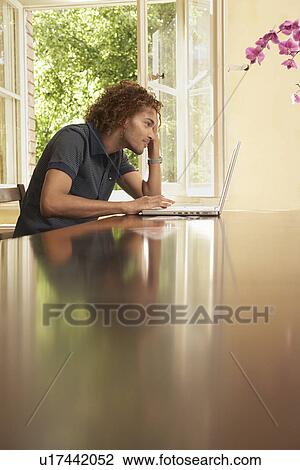Young man using laptop in living room View Large Photo Image Stock Image - Young man using laptop in living room. Fotosearch