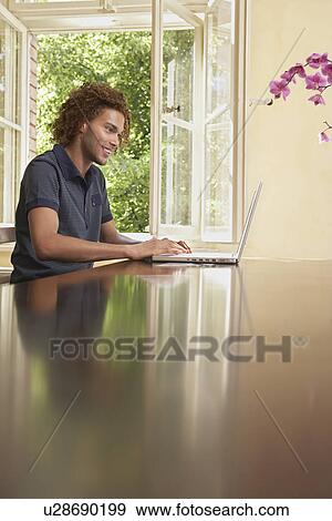 Young man using laptop in living room View Large Photo Image Stock Photo - Young man using laptop in living room. Fotosearch