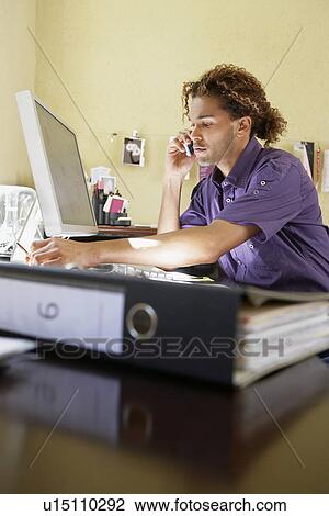 Young man using mobile phone in office View Large Photo Image Stock Image - Young man using mobile phone in office. Fotosearch