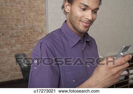 Stock Image - Young man using mobile phone in office. Fotosearch