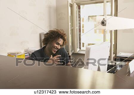 Stock Image - Young man using phone in office. Fotosearch
