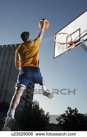 Young man with basketball jumping towards hoop mid-air View Large Photo Image Stock Photograph - Young man with basketball jumping towards hoop mid-air. Fotosearch