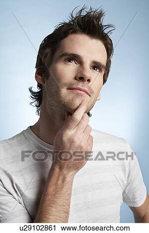 Stock Image - Young man with hand on chin looking up. Fotosearch