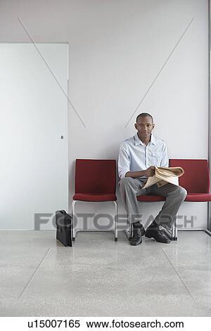 Stock Photography - Young man with newspaper waiting on chairs in corridor portrait. Fotosearch