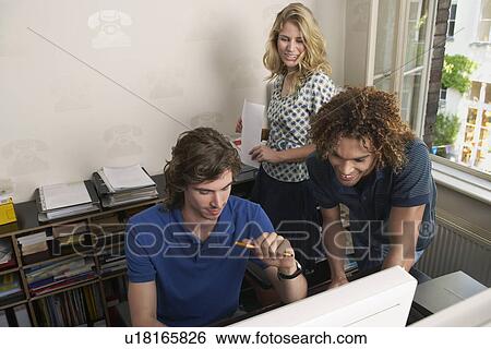 Stock Photograph - Young people looking at computer in office. Fotosearch