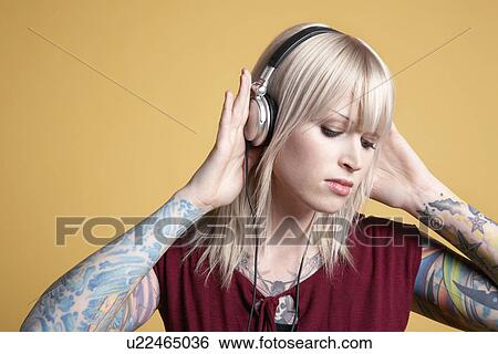 Young tattooed woman listening to music on headphones View Large Photo Image Stock Photograph - Young tattooed woman listening to music on headphones. Fotosearch
