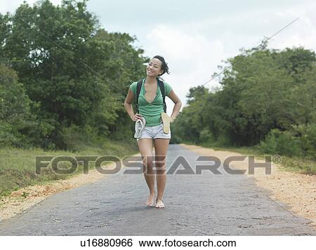 Stock Photograph - Young woman barefoot walking rural road smiling. Fotosearch