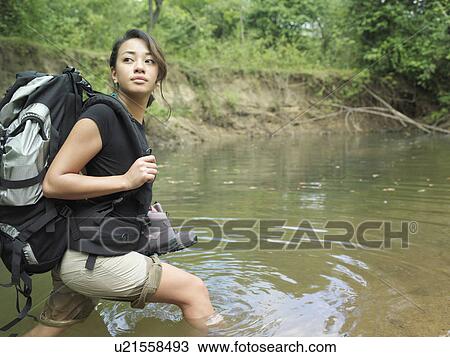 Stock Image - Young woman carrying backpack walking in water looking over shoulder. Fotosearch