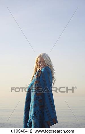 Stock Image - Young woman covered with blanket on beach portrait. Fotosearch
