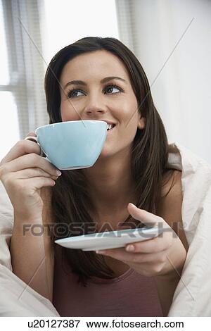 Stock Photo - Young woman drinking tea in bed. Fotosearch