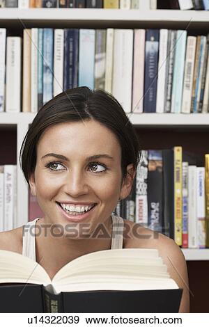 Young woman holding book by bookshelf smiling View Large Photo Image Stock Photo - Young woman holding book by bookshelf smiling. Fotosearch
