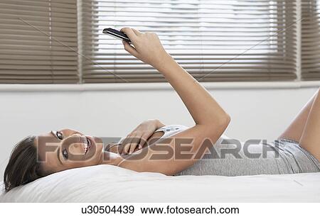 Young woman holding mobile phone lying on bed View Large Photo Image Stock Photo - Young woman holding mobile phone lying on bed. Fotosearch