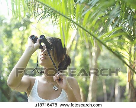 Stock Photo - Young woman in tropical forest looking through binoculars. Fotosearch