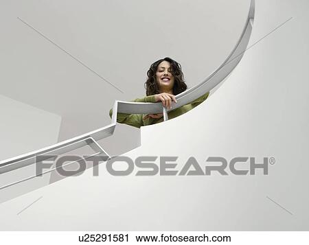 Stock Image - Young woman leaning on railing of staircase low angle view. Fotosearch
