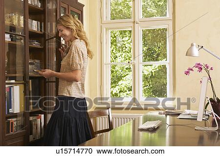 Young woman looking in cabinet in living room View Large Photo Image Stock Image - Young woman looking in cabinet in living room. Fotosearch