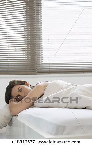 Young woman lying in bed View Large Photo Image Stock Photo - Young woman lying in bed. Fotosearch