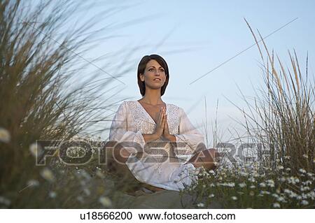 Stock Image - Young woman meditating on sand dune. Fotosearch