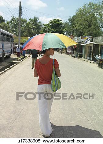 Stock Photography - Young woman on road walking with umbrella back view. Fotosearch