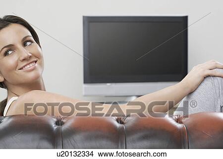 Young woman on sofa in front of flat screen television View Large Photo Image Picture - Young woman on sofa in front of flat screen television. Fotosearch
