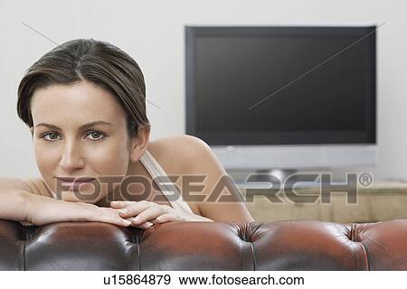 Stock Photo - Young woman on sofa in front of flat screen television portrait. Fotosearch