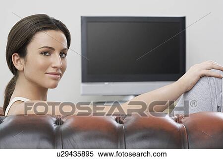 Stock Photography - Young woman on sofa in front of flat screen television portrait. Fotosearch