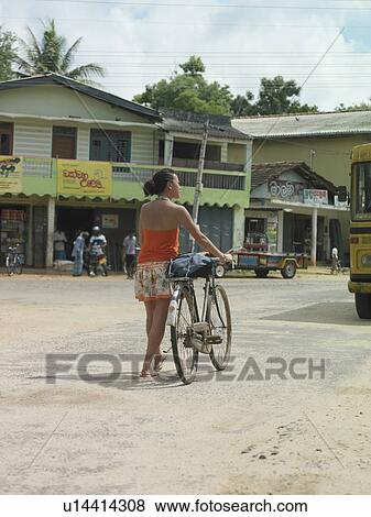 Stock Photo - Young woman on street walking with bicycle back view. Fotosearch