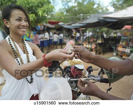 Stock Image - Young woman paying at street market smiling. Fotosearch