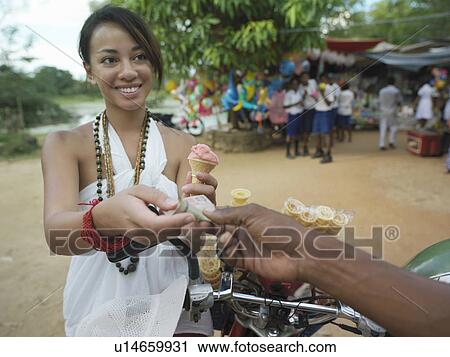 Stock Image - Young woman paying for ice cream at street market smiling. Fotosearch