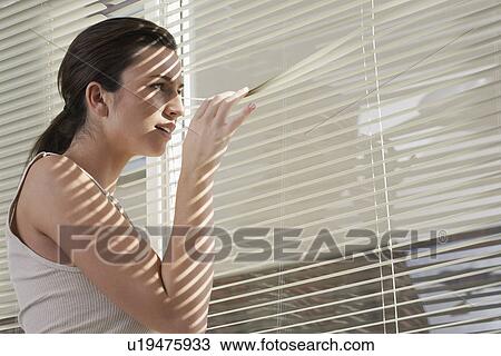 Young woman peering through blinds in home View Large Photo Image Stock Image - Young woman peering through blinds in home. Fotosearch