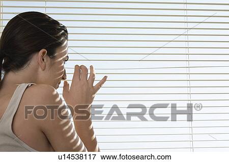 Stock Photo - Young woman peering through blinds. Fotosearch