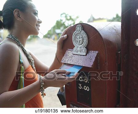 Stock Photography - Young woman putting postcard to mailbox smiling. Fotosearch
