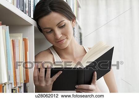 Young woman reading book leaning against bookshelf View Large Photo Image Stock Image - Young woman reading book leaning against bookshelf. Fotosearch