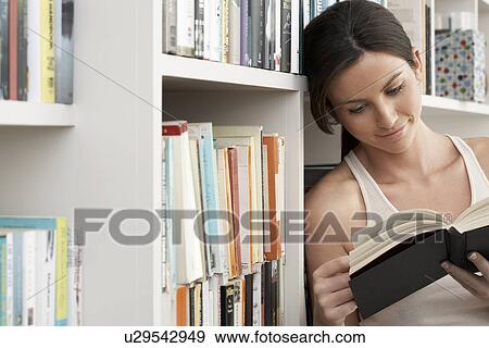 Young woman reading book leaning against bookshelf View Large Photo Image Stock Photo - Young woman reading book leaning against bookshelf. Fotosearch
