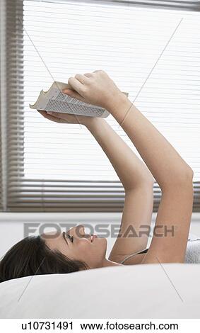 Young woman reading book lying on bed View Large Photo Image Stock Image - Young woman reading book lying on bed. Fotosearch