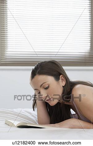 Young woman reading book lying on bed View Large Photo Image Stock Image - Young woman reading book lying on bed. Fotosearch