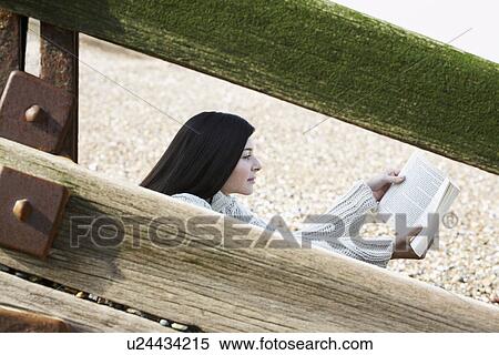 Young woman reading book sitting behind wooden balustrade on beach View Large Photo Image Stock Photography - Young woman reading book sitting behind wooden balustrade on beach. Fotosearch