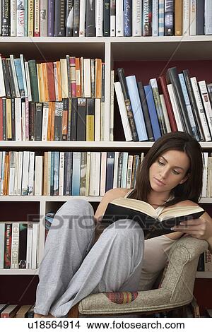 Young woman reading in chair by bookshelf View Large Photo Image Picture - Young woman reading in chair by bookshelf. Fotosearch