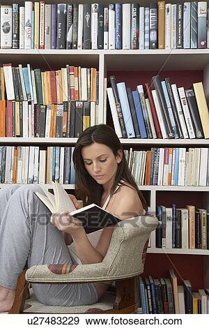 Young woman reading in chair by bookshelf View Large Photo Image Stock Photo - Young woman reading in chair by bookshelf. Fotosearch