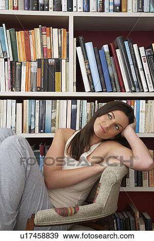 Stock Photo - Young woman relaxing in chair by bookshelf. Fotosearch