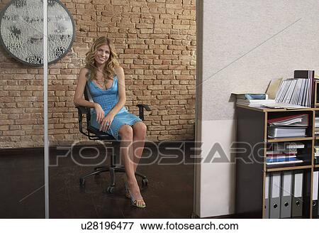 Stock Photo - Young woman sitting in chair in office doorway. Fotosearch