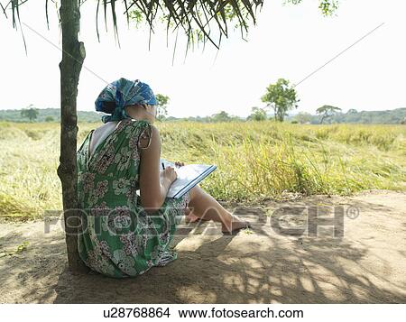 Picture - Young woman sitting in shade writing back view. Fotosearch